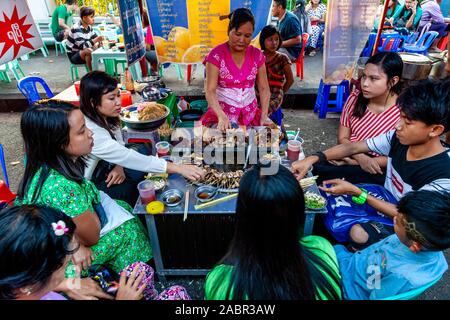 Eine Gruppe junger Menschen essen Essen aus einem Stall in der Innenstadt von Rangun, Yangon, Myanmar. Stockfoto