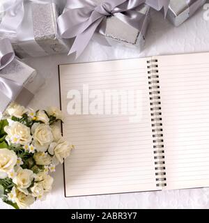 Hochzeit Hintergrund mit gefalteten Notizbuch und Stift auf bridal Spitze mit mehreren Silbernen Hochzeit Geschenke und Rose Bouquet. Platz für Kopieren. Stockfoto