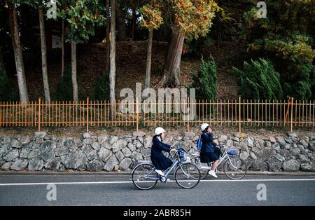 18.November 2014 Okayama, Japan - Junge japanische Mädchen Junior high school Kursteilnehmer auf dem Fahrrad über ruhigen Straße mit grünen treee Hintergrund Stockfoto