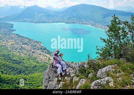 Eine junge Frau sitzt auf dem Felsen und admirring viewview mit Panoramablick auf den See von Annecy vom Mont Veyrier Baron Wanderweg zum Mont, Frankreich Stockfoto