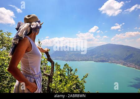 Eine junge Frau mit Hut bewundert einen Panoramablick auf den See von Annecy vom Mont Veyrier Baron Wanderweg zum Mont, Frankreich Stockfoto