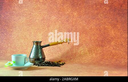 Eine Tasse, schwarz frisch gebrühter Kaffee auf einer Untertasse, in der Nähe eine alte Kupfer Türke in einem Haufen von Kaffeebohnen stehend, Zimtstangen und Anis Sterne. Close-u Stockfoto