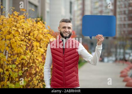 Macht der Worte. Netter junger Mann zu Ihnen schauen, während Sie ein blaues Schild Stockfoto