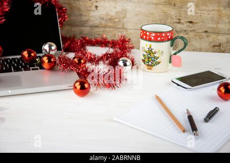 Computer Job an Weihnachten Konzept: Licht Holztisch mit einer offenen Aluminium Laptop, rote Dekoration, rote Kugeln, Weihnachten Tasse Tee, smartp Stockfoto