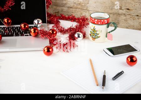 Computer Job an Weihnachten Konzept: Licht Holztisch mit einer offenen Aluminium Laptop, rote Dekoration, rote Kugeln, Weihnachten Tasse Tee, smartp Stockfoto