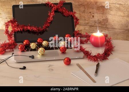 Computer Job an Weihnachten Konzept: ein Aluminium Laptop öffnen, Rot wreath Dekoration, rote und goldene Kugeln, Kerzenlicht, Stift und Lineal auf block n Stockfoto