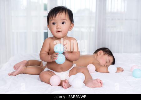 2 Babys auf einem Bett, einer farbigen Kugel, 1 Schlaf Stockfoto