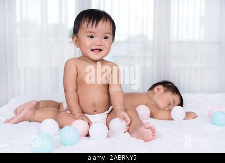 2 Babys auf einem Bett, einer farbigen Kugel, 1 Schlaf Stockfoto