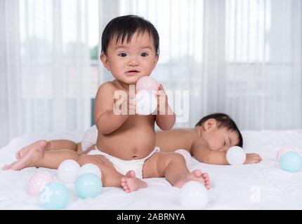 2 Babys auf einem Bett, einer farbigen Kugel, 1 Schlaf Stockfoto