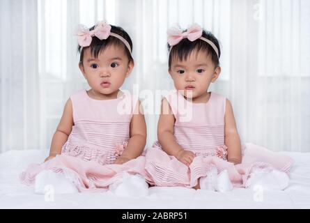 2 Babys in rosa Kleid auf einem Bett. Stockfoto