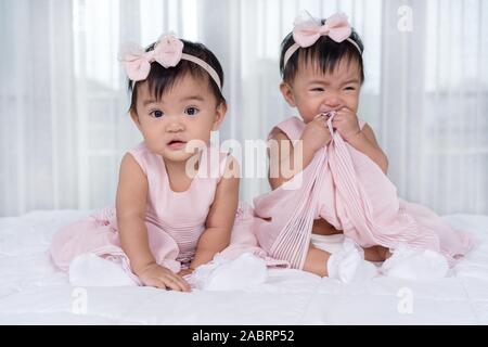 2 Babys in rosa Kleid auf einem Bett, einem suchen, einem weinenden Stockfoto