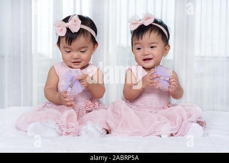 2 Babys in rosa Kleid auf einem Bett. Stockfoto