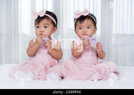 2 Babys in rosa Kleid auf einem Bett. Stockfoto