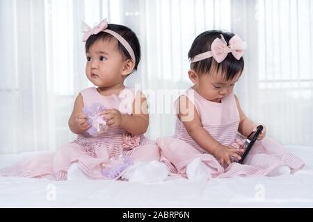 2 Babys in rosa Kleid auf einem Bett, ein smart phone Stockfoto