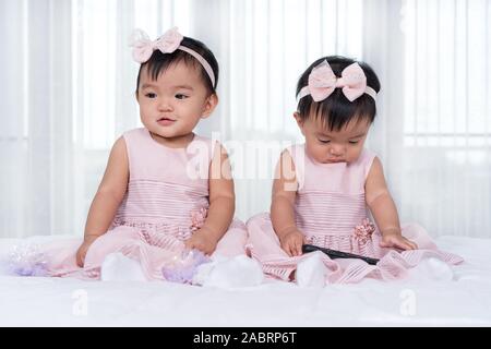 2 Babys in rosa Kleid auf einem Bett, ein smart phone Stockfoto