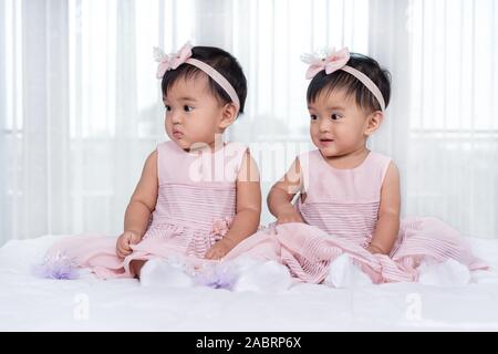 2 Babys in rosa Kleid auf einem Bett. Stockfoto