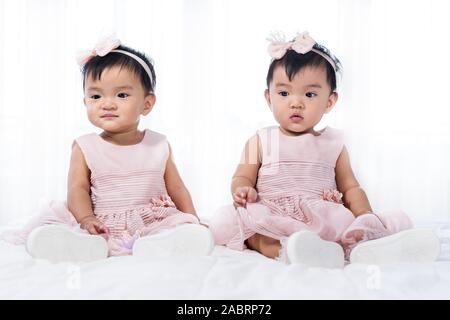 2 Babys in rosa Kleid auf einem Bett. Stockfoto