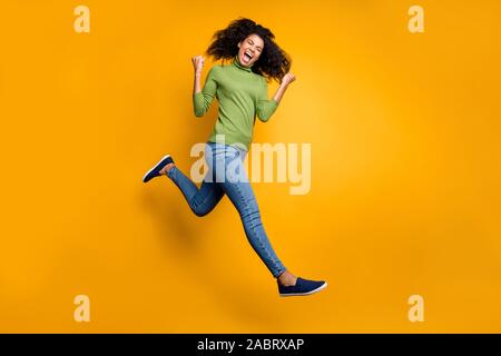 Gedreht in voller Länge Körper Größe Foto fröhliche, positive emotionale Lockig wellig Crazy Mode Mädchen in Jeans Denim grünen Pullover isoliert laufen springen Stockfoto