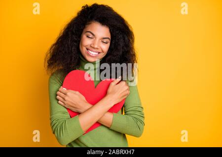 Foto von Lockig wellig zufrieden Zufrieden fröhliches Mädchen in der Freizeit, die begabte Herz lächelnd toothily im grünen Pullover isoliert in leuchtenden Farben. Stockfoto