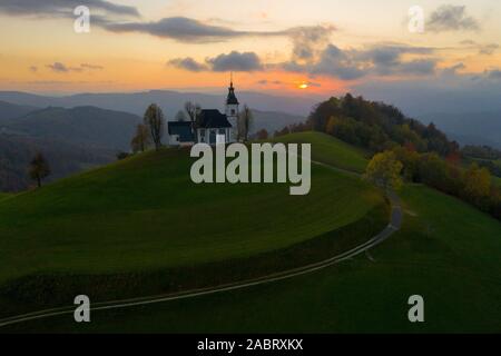 Luftaufnahme der Hügel, bunte Wälder und dem Sv Sobota Kirche. Slowenien Sonnenuntergang im Herbst Stockfoto