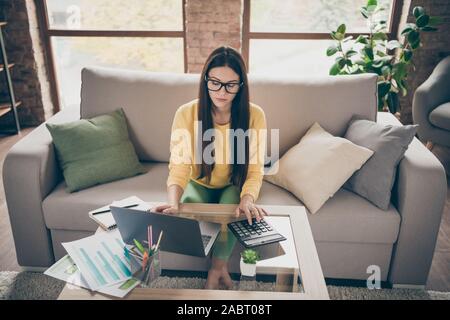 Oben über hohen Winkel Foto des fokussierten Mädchen finanzier Arbeit zu Hause computer Taschenrechner zählen Zahlen verwenden Divan Budget tragen gelbe Jumper drinnen sitzen Stockfoto