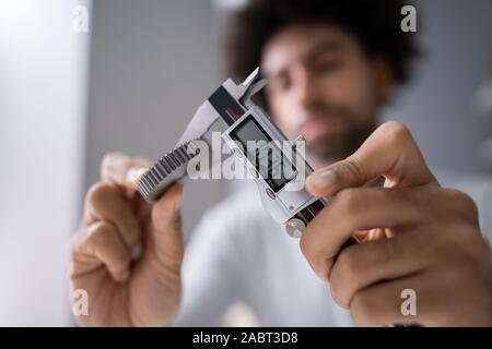 Close-up von der Größe eines Menschen Messgetriebe mit digitalen elektronischen Messschieber auf grauem Hintergrund Stockfoto