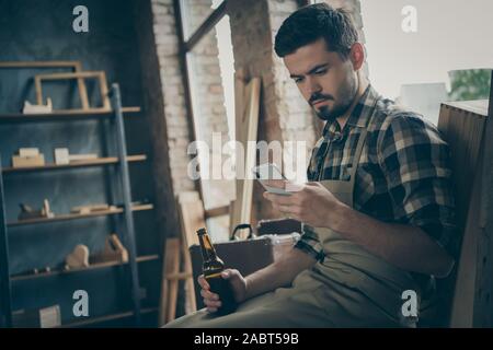 Foto von nachdenklich nachdenklich Mann auf der Suche nach Telefon holding Bier in der Flasche für neue Informationen über Tischlerei Suche Stockfoto