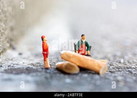 Zwei kleine Müllmänner putzen und fegen Zigaretten auf der Straße, die die Umwelt verschmutzen Stockfoto