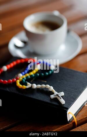 Bunte Rosenkranz, die Heilige Bibel und die Tasse Kaffee. Stockfoto