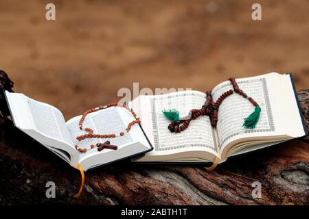Gebetsketten, offene Kuran und offene Bibel auf einer Amtsleitung. Interreligiöse Symbole. Stockfoto