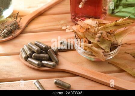 Kapseln und Flaschen von Wesen der natürlichen Medizin mit Heilpflanzen auf hölzernen Tisch. Erhöhte anzeigen. Horizontale Komposition. Stockfoto