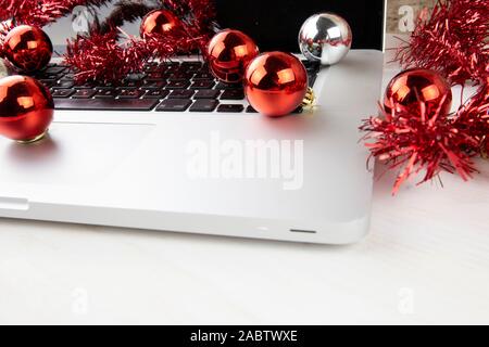 Computer Job an Weihnachten Konzept: Nahaufnahme in Low Angle View aus Aluminium Laptop öffnen, Rot wreath Dekoration und rote und silberne Kugeln auf Stockfoto