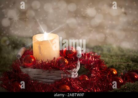 Weihnachten Konzept: Eine brennende Kerze mit Kreuz Bildschirm leuchten Sterne Effekt in einem weißen schäbig Korb mit rote Christbaumkugeln, Rot dekorativer Kranz, natürliche Stockfoto