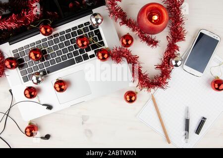 Flach computer Job bei Weihnachtsferien: Blick von oben auf einen hölzernen Tisch mit einer Aluminium Laptop öffnen, Rot Dekoration, rote Kugeln, ein Smartphone, Stockfoto