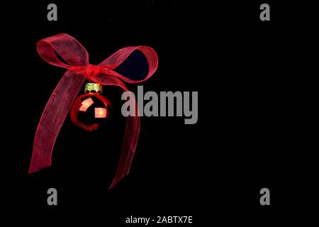 Schwarze Weihnachten Kopie Raum mit roten Ball hängen mit einem rot Organza bow auf schwarzem Hintergrund Stockfoto