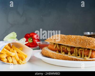 Fast Food essen. Lecker Hot Dog mit Senf und Pommes frites in der Nähe. weißer Tisch und Blu Hintergrund Stockfoto