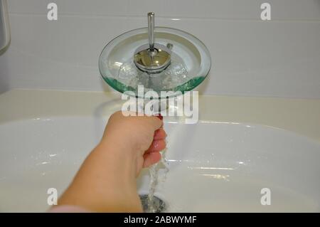 Frau wäscht sich die Hände unter fließendem Wasser. Ein moderner Glashahn, aus dem Wasser im Bad fließt. Stockfoto