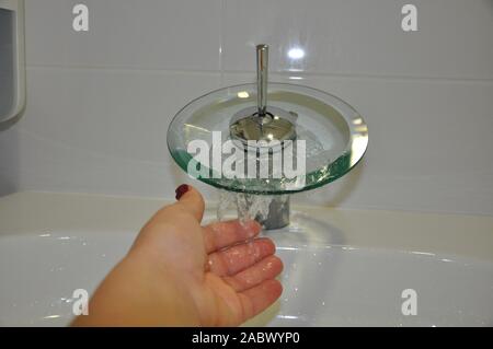Frau wäscht sich die Hände unter fließendem Wasser. Ein moderner Glashahn, aus dem Wasser fließt Stockfoto