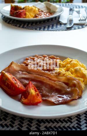 Englisches Frühstück mit gegrilltem Speck, Tomaten, Rührei und gebackene Bohnen in Tomatensoße in Spanien Stockfoto