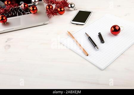 Computer Job an Weihnachten Konzept: Licht Holztisch mit einer offenen Aluminium Laptop, rote Dekoration, rote Kugeln, Smartphone, Block, Stift Stockfoto