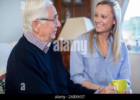 Großvater in ein warmes Getränk und Gespräch mit Erwachsenen Enkelin zu Hause Stockfoto