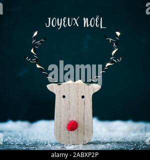 Eine lustige Rentiere aus Holz Kopf, mit einer roten Nase, auf dem Schnee und den Text frohe Weihnachten in Französisch geschrieben Stockfoto