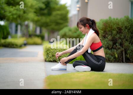 Asiatische schöne Frau sitzend für Entspannen und versuchen, Schnürsenkel in Font ihres Hauses im Dorf, glücklich und Lächeln am Morgen bei Tageslicht. Sport Fitnes Stockfoto