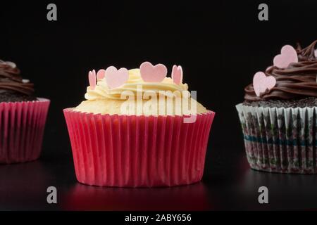 Vanilla Cupcake mit Herzen auf Vereisung zwischen zwei chocolate Cupcakes, schwarzer Hintergrund Stockfoto