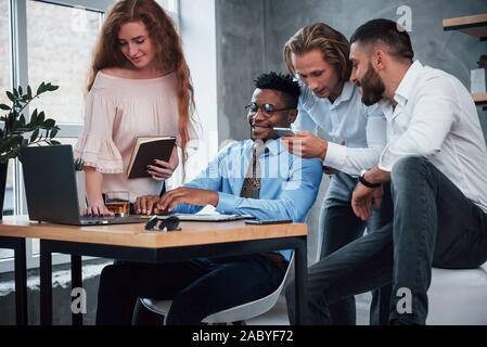 Besprechen Sie ihr Smartphone und Laptop arbeiten. Gruppe der multirassischen Büroangestellte in formelle Kleidung sprechen über Aufgaben und Pläne Stockfoto