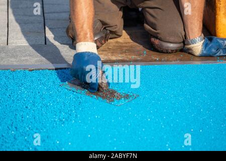 Mason Nivellierung Gummibeschichtung für Spielplätze mit Kelle, Maurer hand verbreiten Krümel aus weichem Gummi. Outdoor weiche Beschichtung und Bodenbelag für Sport Stockfoto