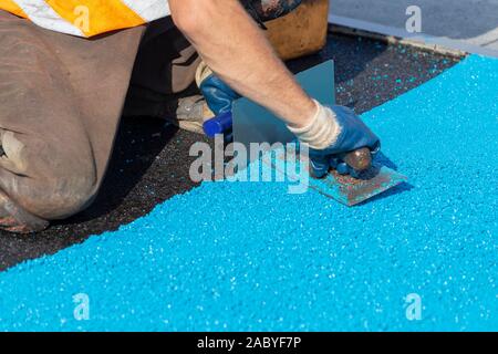 Mason Nivellierung Gummi mulch Beschichtung für Spielplätze und Sport, auf der Oberfläche von einem Stahl Kellen angewendet. PDM Gummigranulat. Selektive konzentrieren. Stockfoto