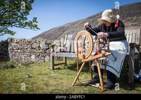 Eine ältere Frau trägt einen Hut gegen die Sonne dreht Schafwolle mit einer manuellen Spinnrad, Sangerhausen, Schottland Stockfoto