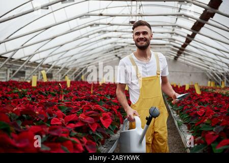 Zusehen und lächelnd. Portrait von schönen jungen Kerl im Gewächshaus die Pflege von Blumen Stockfoto