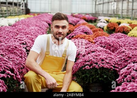 Ein zwischen dieser Schönheit sitzen. Foto von schönen jungen Kerl im Gewächshaus die Pflege von rosa gefärbten Blüten Stockfoto